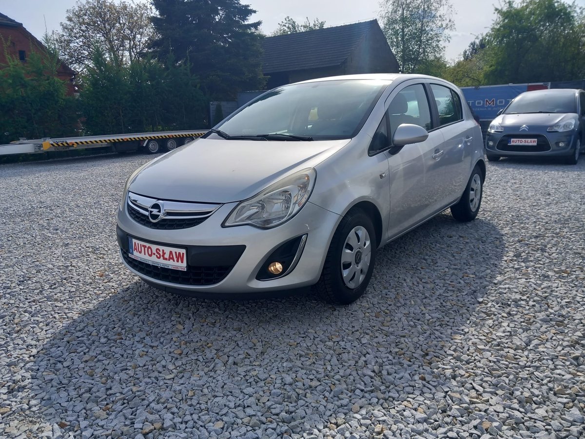 White Opel Corsa compact car parked on gravel lot with other vehicles and trees in background