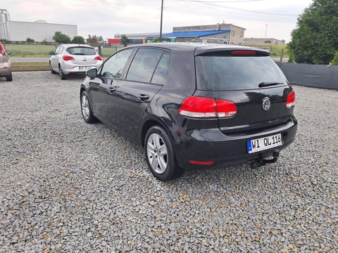 Black Volkswagen Golf parked on gravel lot with other vehicles and buildings visible in background