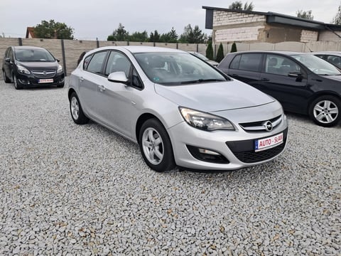 White Opel Astra hatchback in a car lot with other vehicles and buildings in the background