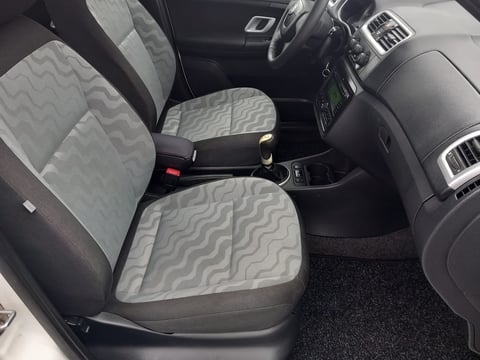 Interior view of car with gray and black quilted seat covers, steering wheel, dashboard controls, and center console armrest