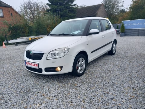 White Skoda compact family car parked on gravel lot with brick building and trees in background