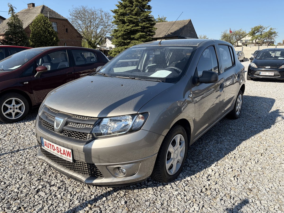 Silver Dacia Sandero parked in outdoor lot with other vehicles and residential houses visible in background