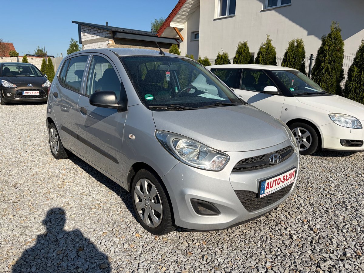 Silver Hyundai i10 hatchback with roof rack parked in outdoor lot with other vehicles and residential building in background