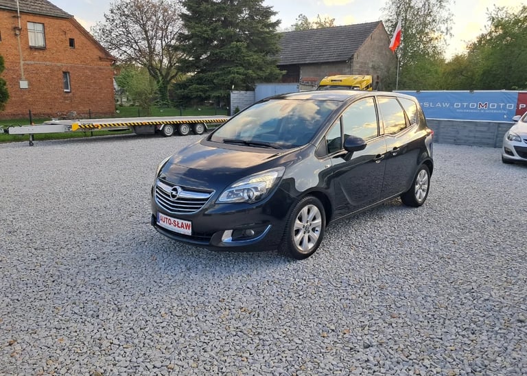 Black Opel Meriva compact car parked in driveway with brick buildings and landscaping in background