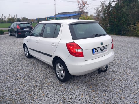 White compact hatchback car parked on gravel lot with dark vehicle visible in background