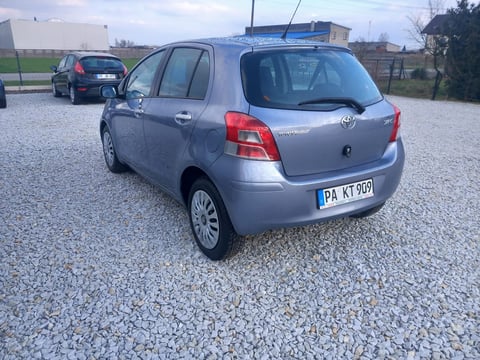 Silver Toyota Yaris compact car parked on gravel lot, rear view visible with blue roof rack